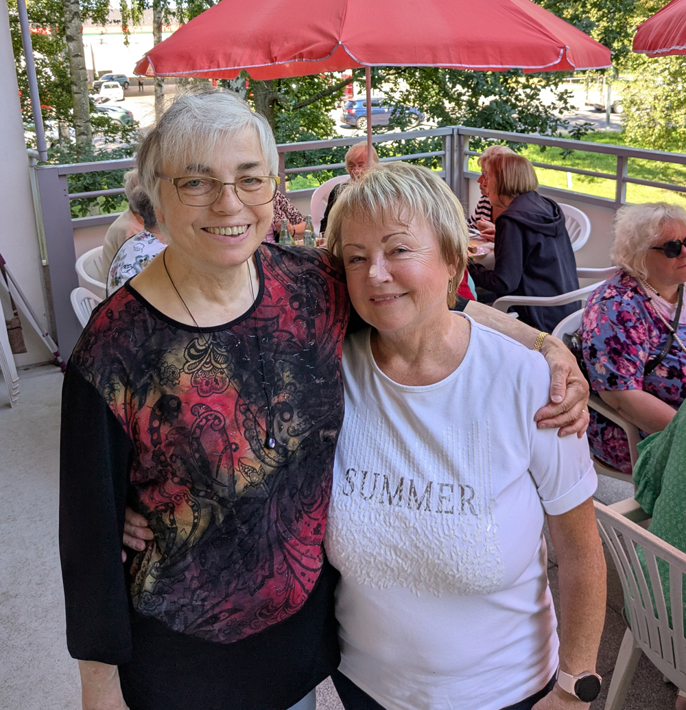 Zwei Frauen stehen lächelnd Arm in Arm auf der Terrasse
