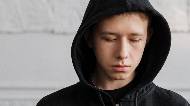 Ein Junge mit dunklem Kapuzenpullover schaut nachdenklich auf den Boden.